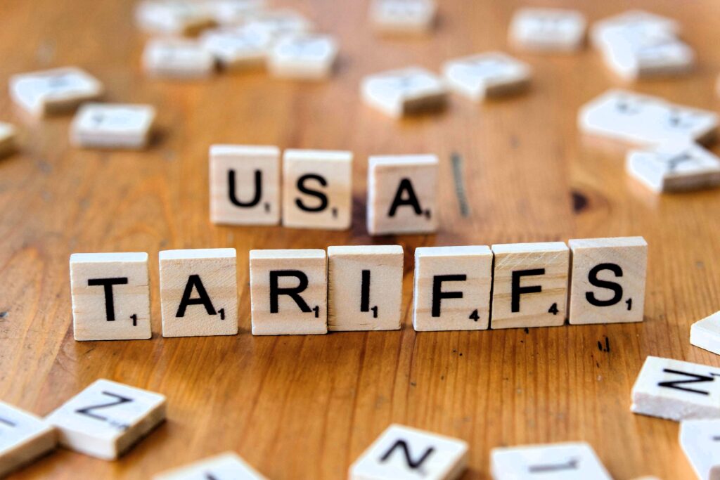Wooden Scrabble tiles spelling out "USA TARIFFS" on a wooden surface, representing trade or economic policies.