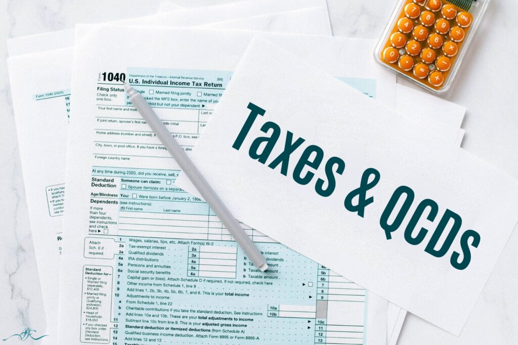 ax forms and calculator on a desk with a pen and paper labeled ‘Taxes & QCDs,’ representing the tax aspects of Qualified Charitable Distributions.