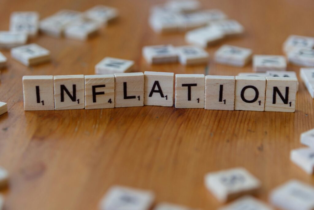 Wooden letter tiles spelling the word “inflation” arranged in a row on a table, with blurred letter tiles scattered in the background, illustrating rising prices in the context of the U.S. economic outlook 2026.