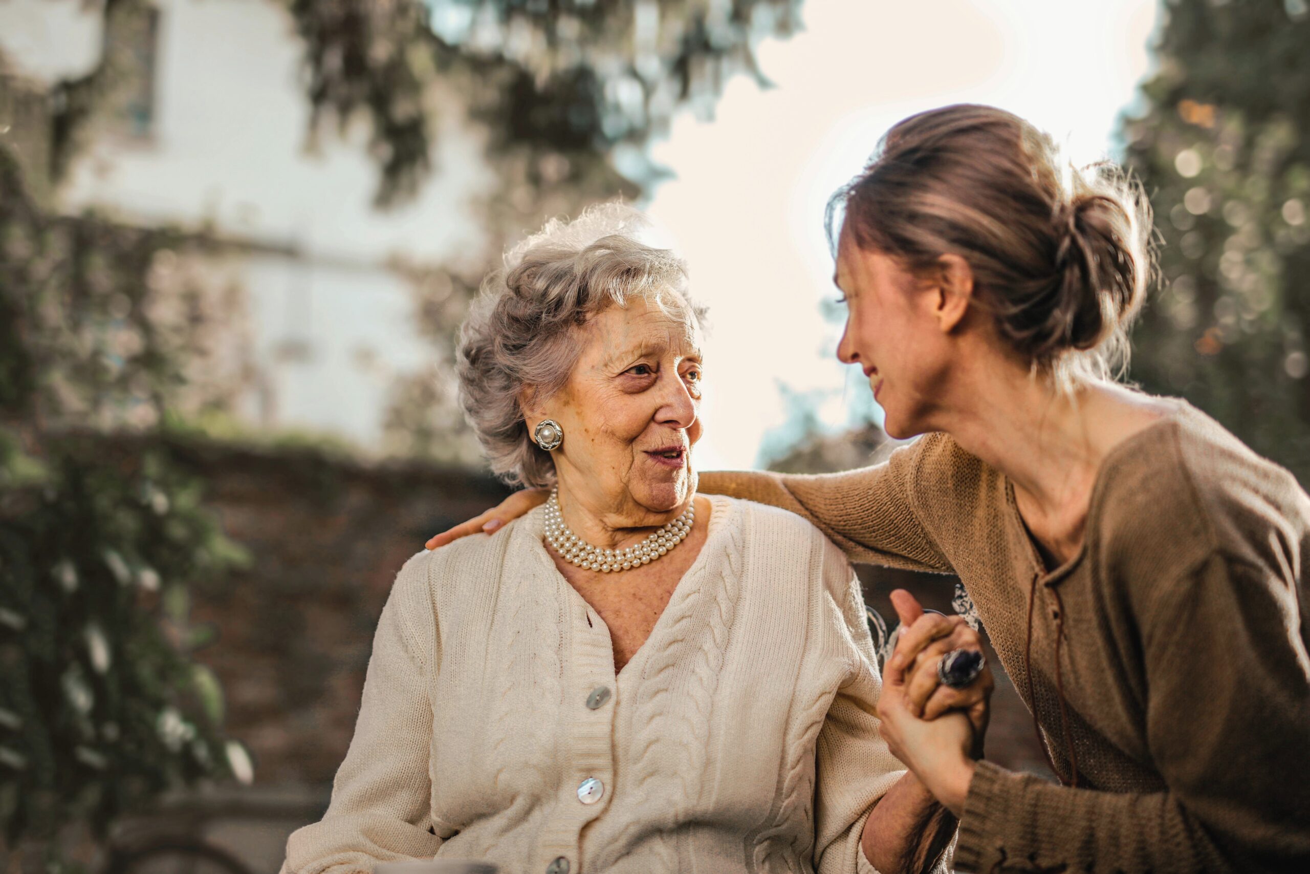 Adult daughter gently holding her elderly mother’s hand outdoors, sharing a supportive conversation about assisted living and future care choices.