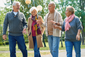 Four older adults walking together in a park, smiling and talking, illustrating the benefits of social connection for brain health and healthy aging.