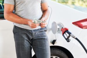 man holding handful of cash next to car being filled at gas station
